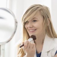 Girl applying makeup in front of mirror at home